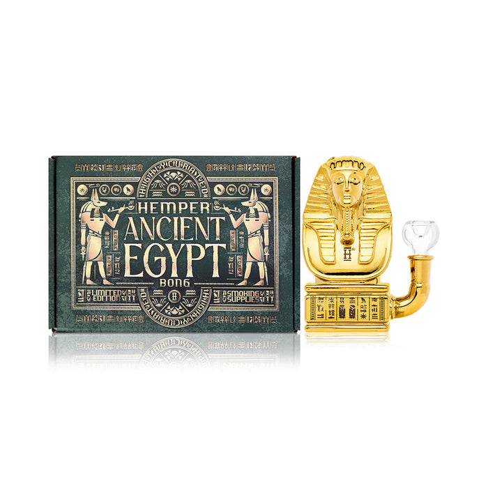 Front hero shot of Hemper Ancient Egypt mini glass bong next to decorative box, highlighting gold finish and compact size.