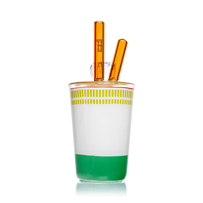 Rear angle of Hemper ramen cup bong showing white and green graphics, yellow lid and paired amber glass chopsticks.