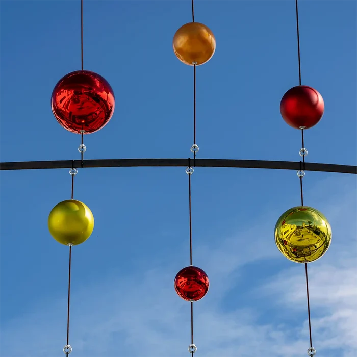 Large shiny red, gold, and green shatterproof ornaments suspended over an outdoor walkway