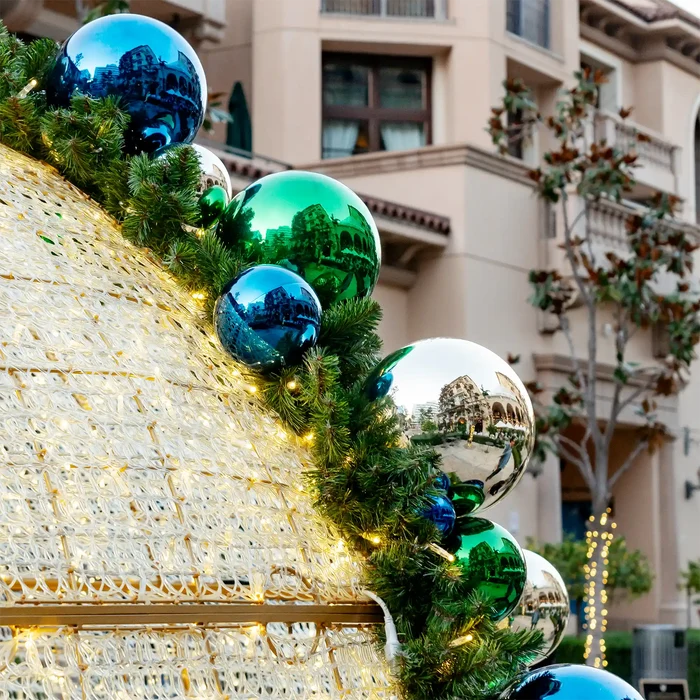 Large shiny blue, green, and silver shatterproof ornaments on a lighted outdoor Christmas display