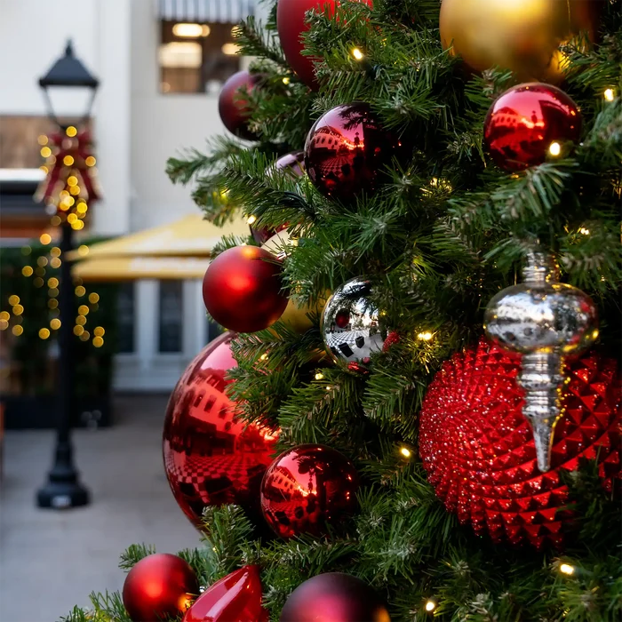 Large shiny red, gold, and silver shatterproof ornaments on a decorated Christmas tree